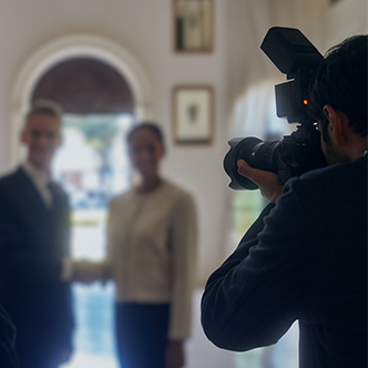 A photographer standing in front of a man and a woman shaking hands, capturing the moment.