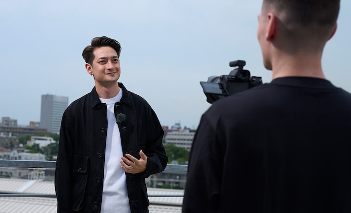 Usage image of a man hand-holding a camera, shooting footage of another man with an ECM-L1 microphone in an outdoor setting