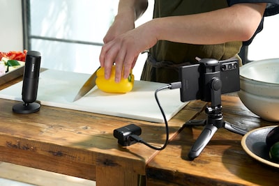 Usage image showing a person cooking with the microphone standing nearby, with the receiver connected to a smartphone on a stand via a USB cable