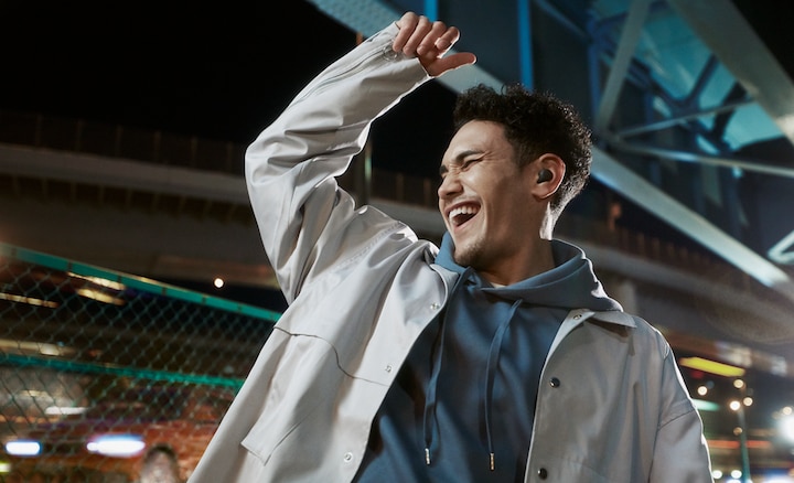 Split screen image of a man dancing in a stadium environment wearing LinkBuds S with Ambient Sound Mode on and arm raised