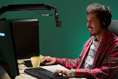 Usage image of a man wearing headphones connected by cable to a microphone while sitting in front of a PC monitor screen