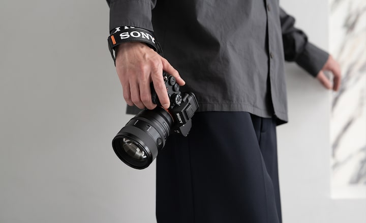 With the FE 85mm F1.4 GM II mounted on the α7R V, the image depicts a man effortlessly carrying it with one hand.