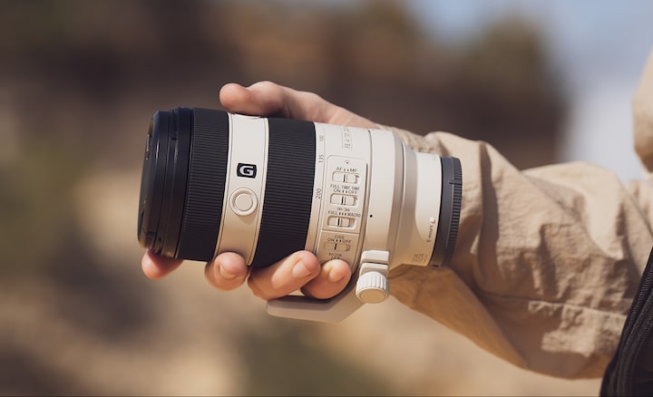 Usage image showing lens body held in palm of user’s hand, emphasising compact size